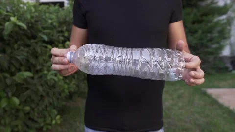 Slow Motion hip level shot of a man showing a plastic bottle at his backyard  動画素材 139872853