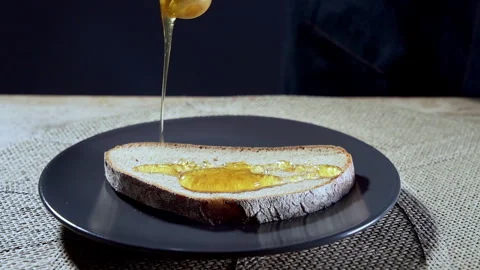 Slow motion. Honey flowing onto a slice of dark bread. Stock Footage 295379805
