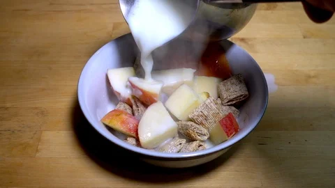 Slow motion: Hot milk being poured onto a bowl of wheat and apple cereal. Stock Footage 87330918