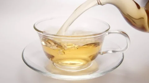 SLOW MOTION: Hot tea flowing to a tea cup from a teapot - side view Stock Footage 70572888