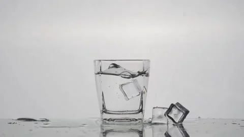 Slow-motion Ice Cube Drop into Crystal Clear Glass - White Background Stock Footage