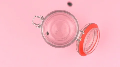 Slow motion image of black beans falling on jar glass over pastel background. Video stock 106807100