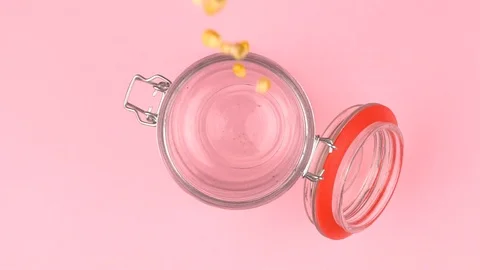 Slow motion image of popcorn falling on jar glass over pastel background. Video stock 106806615