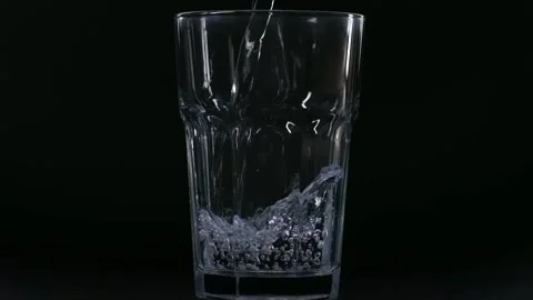 Slow motion jet of water pours into the glass on the table. On a black Stock Footage 233981966