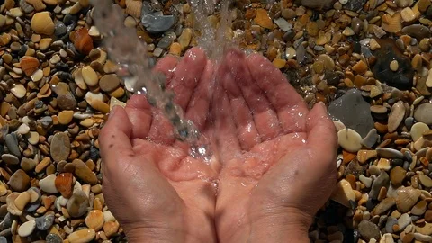 Slow motion of jet waterfall and splash on woman hands on pebble beach Stock Footage 98102449