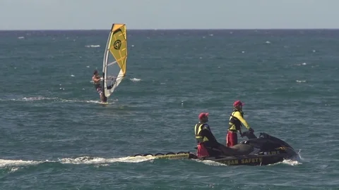 Slow Motion Jetski with lifeguards patrolling with windsurfer in background Stock Footage 77611045