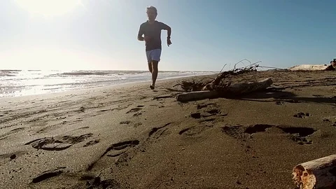 Slow Motion Jogger on a sand beach run near the sea at sunset Stock Footage 87560360