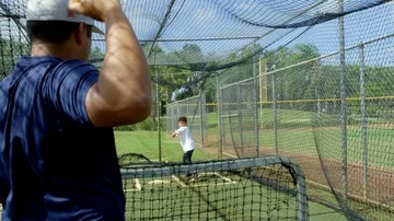 Slow motion of kid being thrown a baseball by coach inside batting cages Stock Footage 85653657