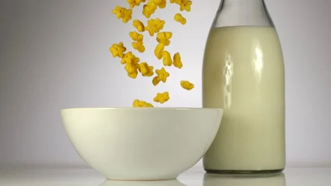 SLOW MOTION: Kid corn flakes falling in a white dish near a milk on a table Stock Footage 108959663