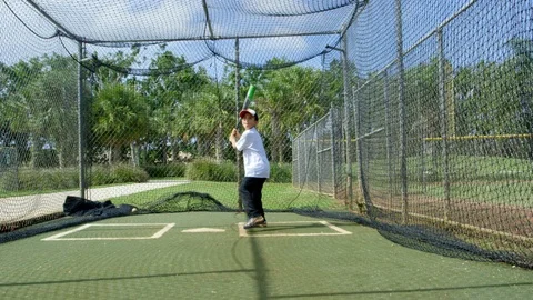 Slow motion of a kid hitting baseball inside batting cages at park Stock Footage 85642759