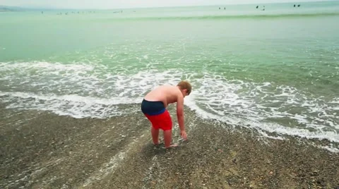 Slow motion of kid picking up sand and throwing it by ocean at beach Stock Footage 63749990