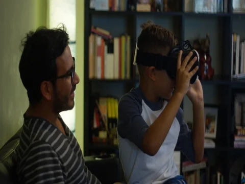 Slow Motion of kid sitting in his father's lap playing with VR headset Stock Footage 78490955