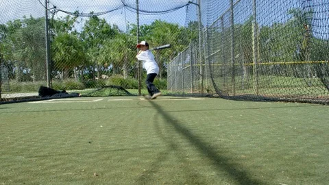 Slow motion of kid swinging at ball inside batting cages at baseball park Stock Footage 87811042