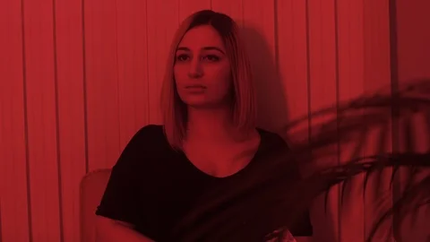 Slow motion lady in black dressing sits under red light Stock Footage 105249875