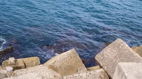Slow-motion large concrete blocks by shoreline with deep blue sea in background Stock Footage 321477187