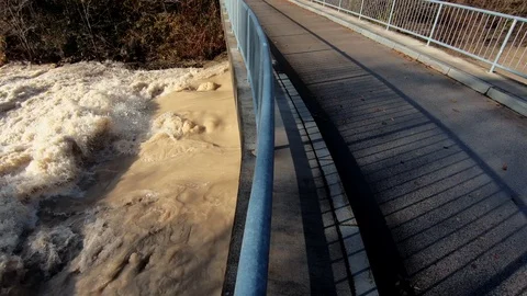 Slow motion left pan small road bridge over wild chaotic flooded river Stock Footage 121679762