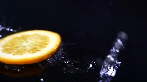 Slow motion lemon falling with water drops on black surface. Video stock 60952996