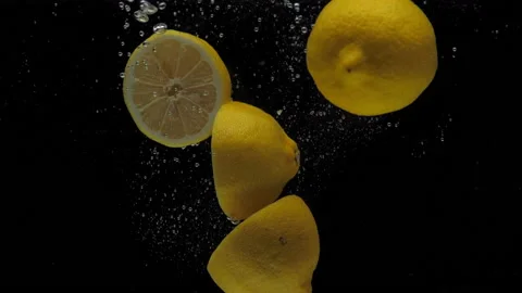 Slow motion lemon halves falling into transparent water on black background Stock Footage 164461599