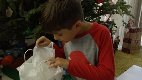 Slow motion of a little boy in front of Christmas tree looking inside a gift Stock Footage 88469590