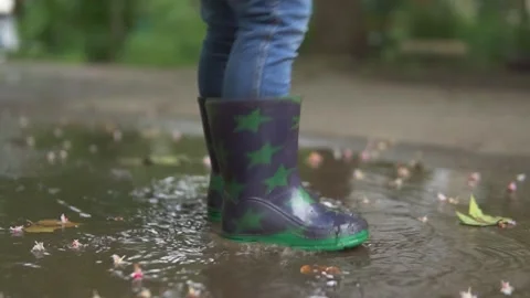 SLOW MOTION, LOW ANGLE, CLOSE UP, DOF: Carefree little boy in grey rain boots Stock Footage 155010703