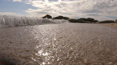 Slow motion, low angle shot of waves breaking on beach with rocks on horizon Video stock 132936870