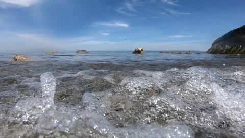 Slow motion low angle waves hitting rocky shore on bright sunny day Stock Footage 130072770