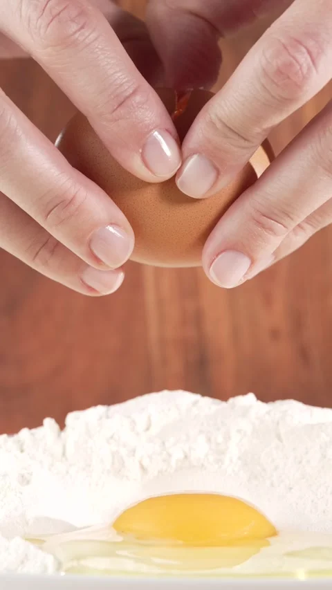 Slow motion macro of female hands cracking an egg over flour with an egg al.. Vídeos de archivo 312169758