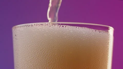 Slow motion macro shot of pouring bright yellow beer from bottle into a glass Stock Footage 246477088