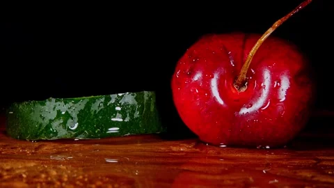Slow motion macro of water droplets spraying on green cucumber and red cherry Stock Footage 324273160