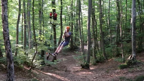 Slow motion of a man with a beard and a helmet descending from a small ziplin Stock Footage 129347263