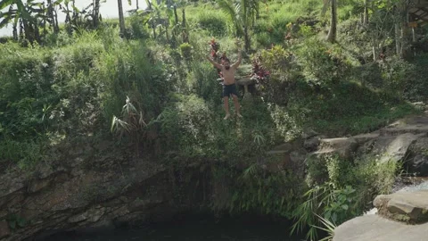 Slow motion of a man cliff jumping into a natural river pool in Bali Stock Footage 313353316