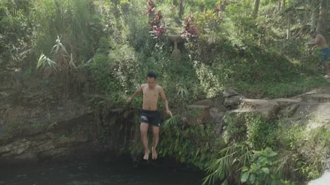 Slow motion of a man cliff jumping into a natural river pool in Bali Video stock 313353627