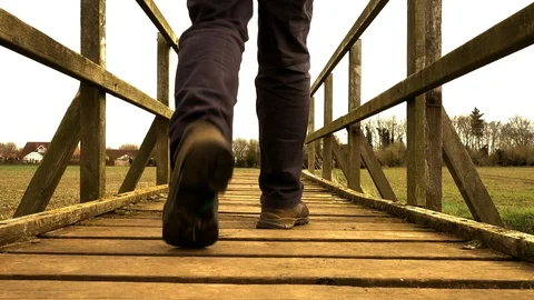 Slow motion – Man crossing an old wooden bridge (rear view). Video stock 104971565
