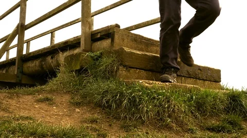 Slow motion – Man crossing old wooden bridge then descending steps (front view). 스톡 동영상 104972279