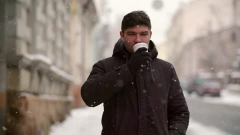 Slow motion man drinking coffee in early morning snowing city. Young tourist Stock Footage 261340858