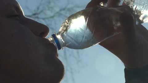 Slow Motion. A Man Drinks Water from a transparent Plastic Bottle against a Blue Video stock 153099251