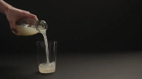 Slow motion man hand pour lemon ginger lemonade into tumbler glass on black Stock Footage 325070192