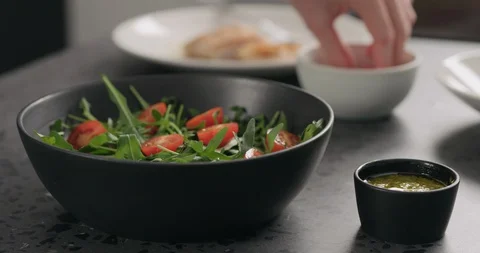 Slow motion man hands put cherry tomatoes over fresh arugula in black bowl on Stock Footage 128647744