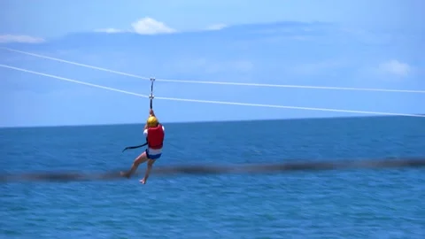 Slow motion of man having fun at zipline, sliding in front of blue sky Stock Footage 142463375