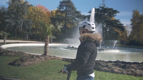 Slow Motion of Man with Helmet Using Electric Scooter in Park with Fountain 1 Vidéo 98757254