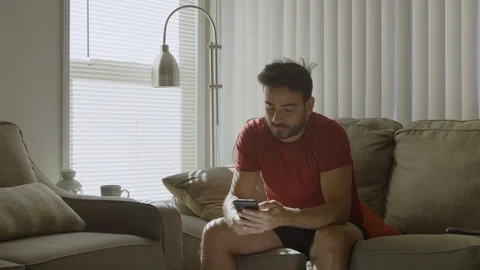 Slow motion of man at home scrolling on cell phone and looking bored Stockbeeldmateriaal 114645052