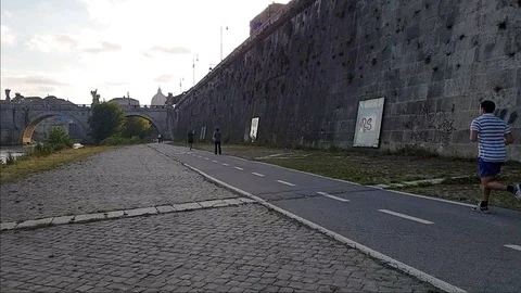 Slow Motion A man jogs In Rome near the Tiber river with view of St. Peter dome Stock Footage 108503034