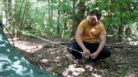 Slow motion of man pitches a tent at a campsite in the woods but fails to Stock Footage 206045160