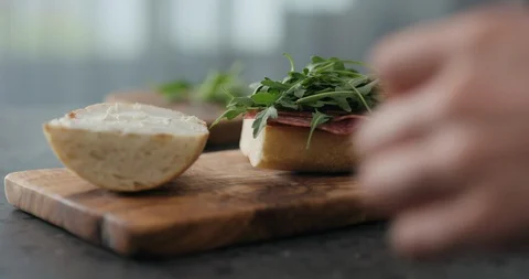 Slow motion man put top on ciabatta slice on olive board Video stock 119882262