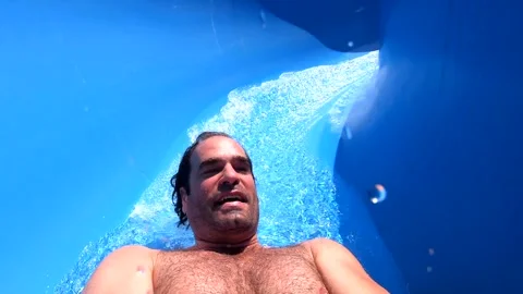 Slow motion of a man riding down slide in aqua park and falling into water Video stock 242420544