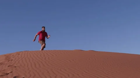 Slow motion of man running and jumping down the face of a sand dune Stock Footage 64696528