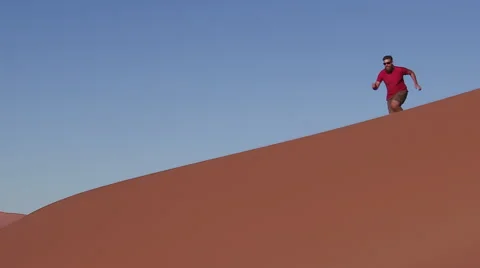 Slow motion of man running and jumping down the face of a sand dune Stock Footage 64710860