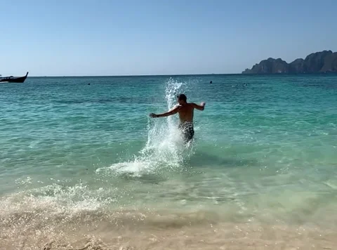 Slow motion of a man running on a white sandy beach into azure water Video stock 219857265