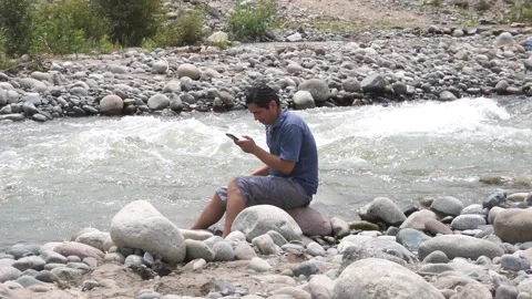Slow motion of a man sitting on a stone looking at his cell phone Stock Footage 150954342