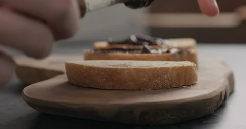 Slow motion man spreading chocolate spread on ciabatta slice on olive board Video stock 128645785